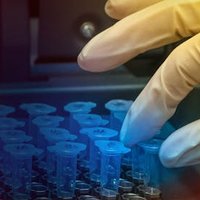 Gloved hand picking up test tubes.
