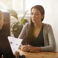 Two ladies chatting over a desk. One lady is holding documents.