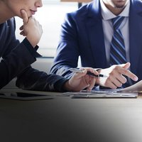 Closeup image of man in a suit pointing to what's written on paper while a student looks on.